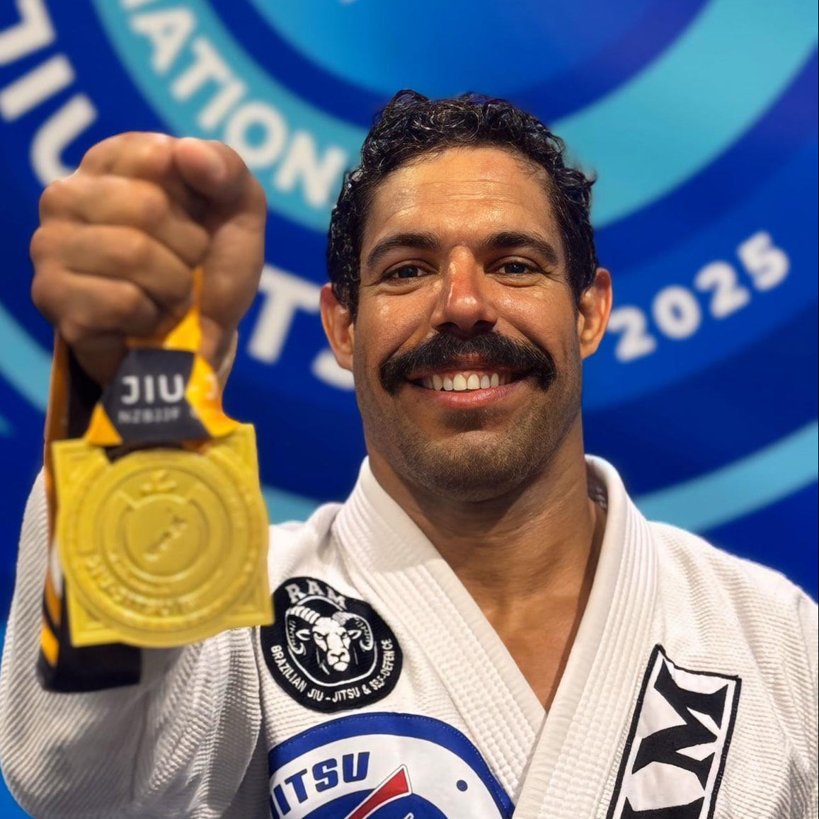 Professor Tiago in a white martial arts uniform holding a gold medal.